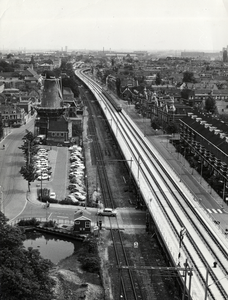 168535 Overzicht van de nieuwe, verhoogde spoorbaan door Delft, met links ervan het oude, lage (hulp-)tracé.